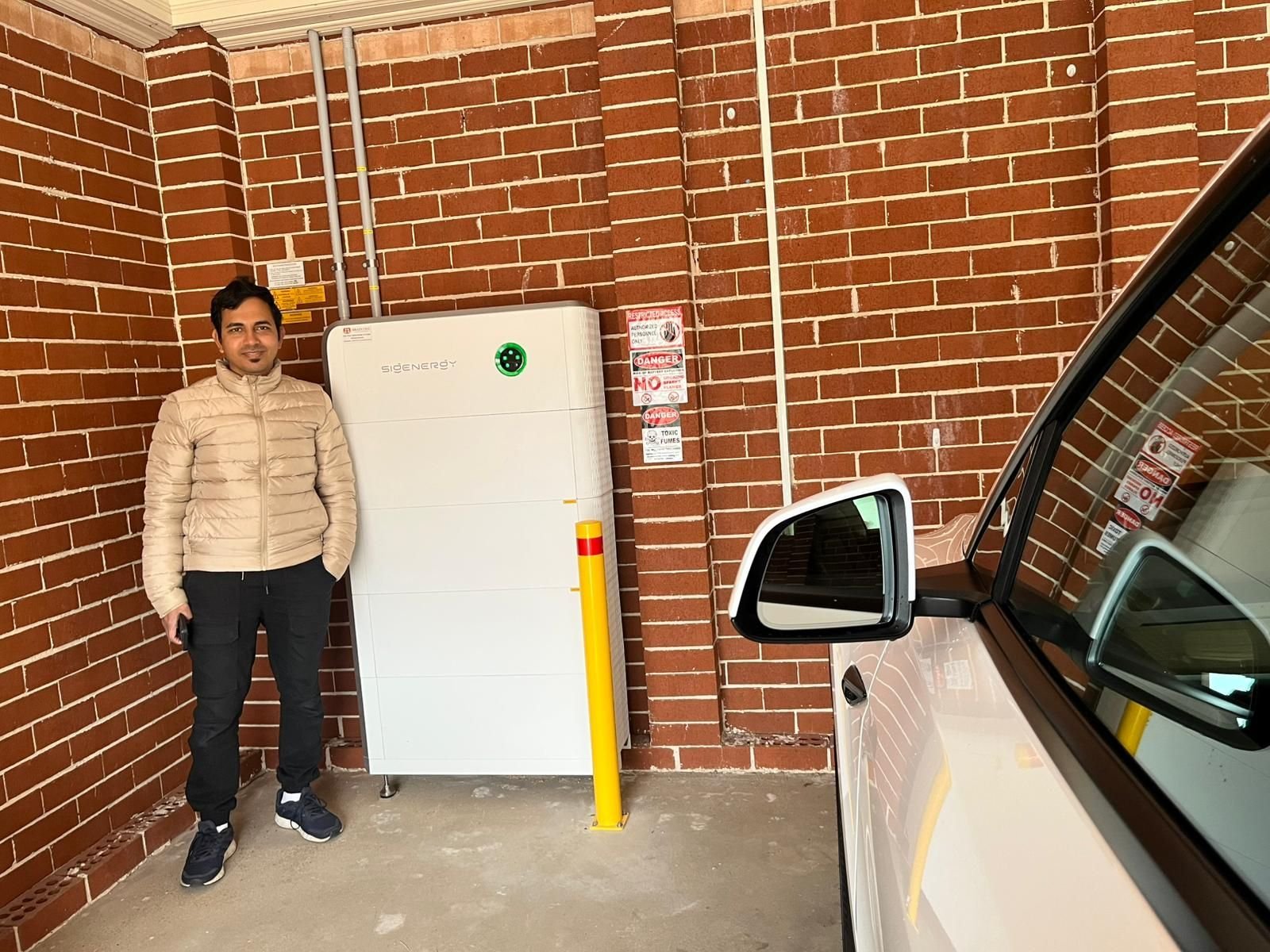 Mahmud standing in his carport next to his newly installed Sigenergy home battery stack
