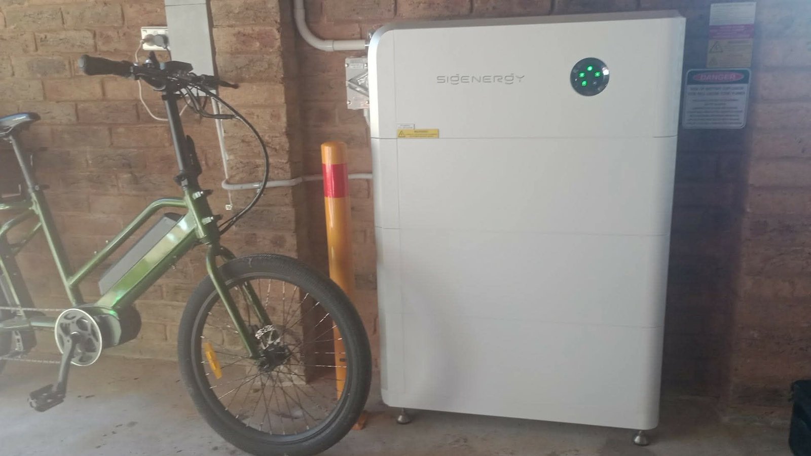 The Sigenergy battery stack standing in the garage next to the family's green e-bike