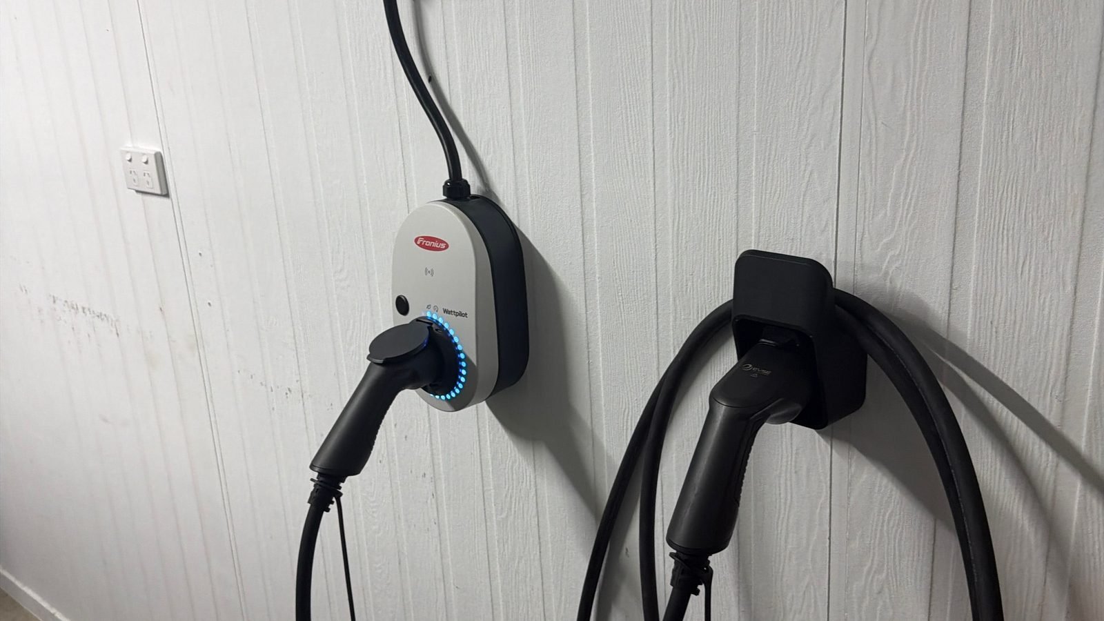 A wall-mounted Fronius Wattpilot EV charger and cable holster beside a standard Australian power point