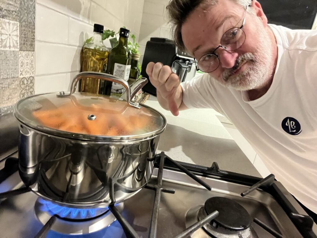Man in glasses giving a thumbs-down beside a saucepan on a lit gas burner