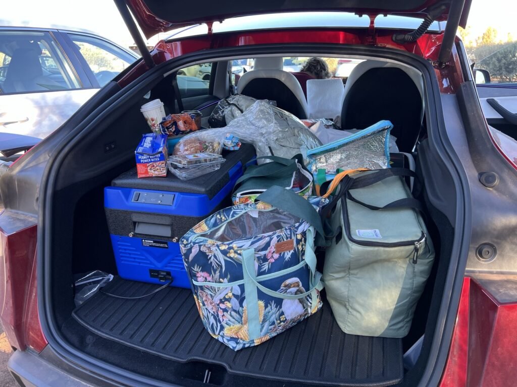Open boot of a red Tesla Model Y packed with a blue 12-volt fridge, cooler bags and snacks