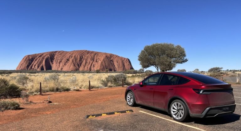 Red Tesla Model Y with TRIPNG plates parked in front of Uluru under a clear blue sky