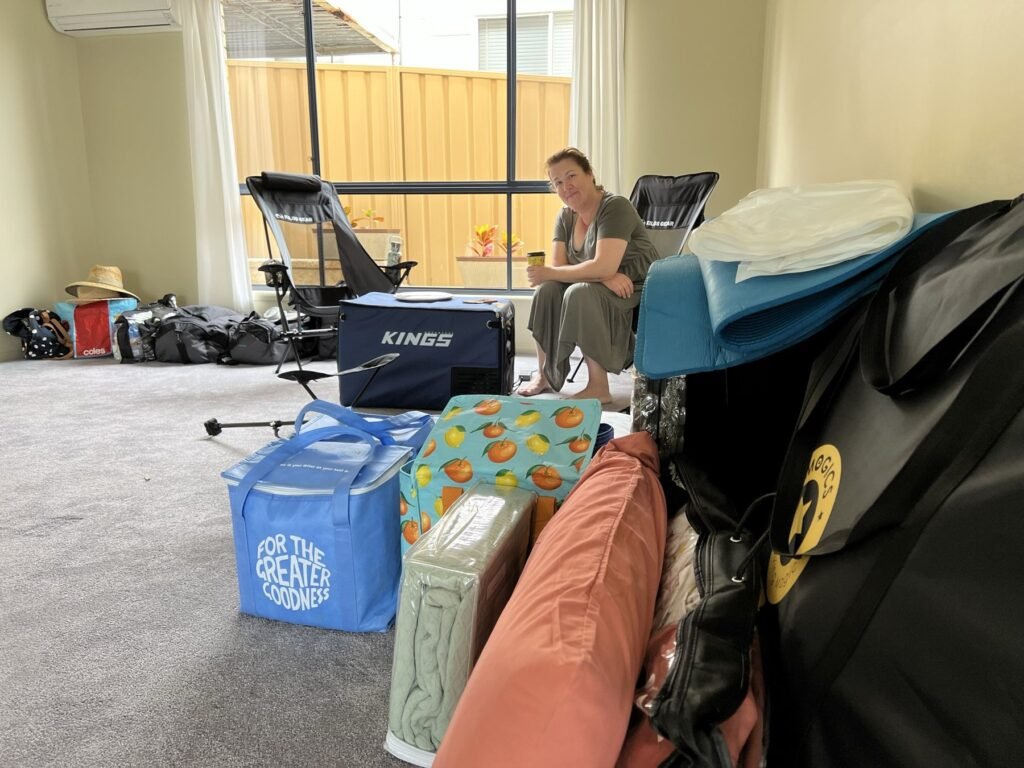 Camping chairs, a 12-volt fridge, bedding and bags laid out on the floor of an empty living room